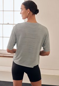 Helehall toonis kerge sportlik särk lõdva lõike ja lühikeste varrukatega, mida kannavad mustad jalgrattapüksid. Materjalil on peen tekstuur ja läige.