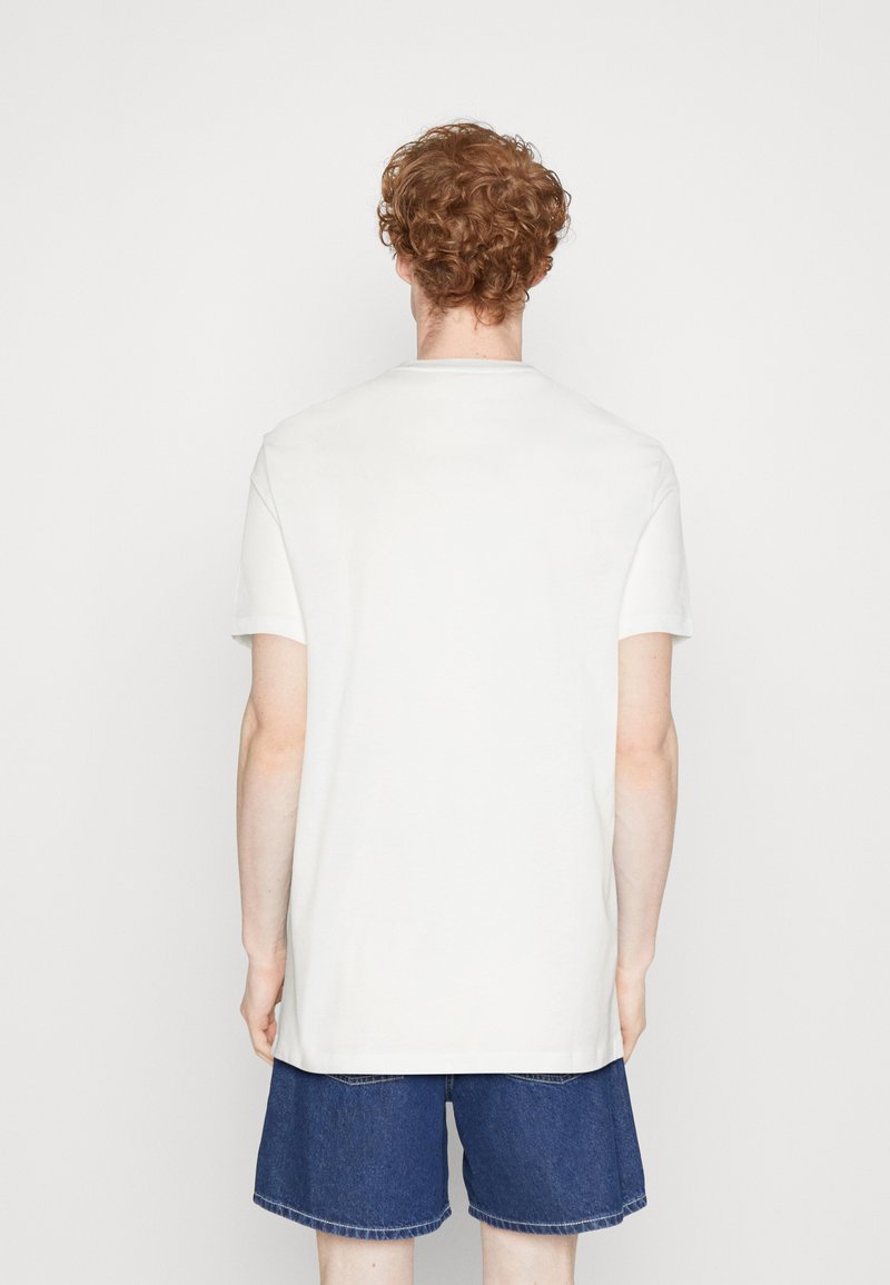 Camiseta de algodón blanca de manga corta y cuello redondo, vista desde la parte de atrás, combinada con pantalones cortos de mezclilla. Diseño sencillo, sin patrones ni acentos.