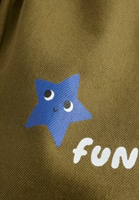 Barna textúrájú anyag, melyen egy kék csillag grafika látható, szemekkel és mosolygó számmal, mellette pedig a "fun" szó fehér színben.