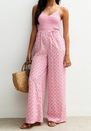 Vaaleanpunainen kuvioitu haalari, jossa on vartalonmyötäinen yläosa, leveälahkeiset housut ja säädettävät spagettihihnat. Kudottu laukku täydentää asun.