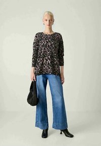 Blusa oversized com padrão de leopardo em preto e rosa, com mangas de três quartos, combinada com jeans de perna larga e botas de tornozelo pretas de salto.