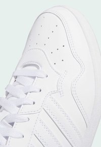 Hvid sneaker med syntetisk overdel, perforeret tå og tekstureret sål. Har flade snørebånd og tre sidelange striber for en ekstra detalje.