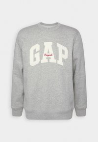Felpa grigia realizzata in morbido tessuto con collo rotondo. Presenta "GAP" in bianco e "Original" in rosso sul davanti. Nessun motivo o dettaglio.