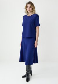 Ensemble composé d'un haut et d'une jupe bleu marine en tissu doux ; manches courtes, coupe décontractée. Jupe longueur genou avec une silhouette trapèze. Associé à des bottes noires mi-mollet.
