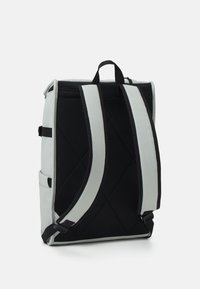 Mochila rectangular gris con panel trasero de malla acolchada negra y correas de hombro ajustables grises con ribete negro, de pie sobre un fondo blanco.