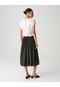 Haut blanc à manches courtes associé à une jupe noire avec un motif géométrique, un design évasé et une taille. Texture de tissu lisse.