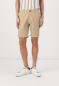 Khaki shorts with a straight fit, featuring a button closure, side pockets, and a rolled hem. Paired with white sneakers.