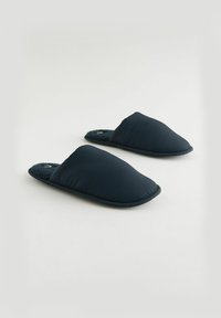 Pantoufles bleu marine avec un dessus rembourré, une doublure en polaire douce et une semelle plate. Le design présente une forme de bout arrondi simple.
