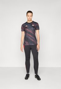 Zwarte en rode sportshirt met abstract ontwerp, korte mouwen en logo, gecombineerd met zwarte leggings met rode zijaccenten en zwarte sportschoenen.