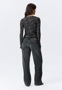 Μαύρο μακρυμάνικο τοπ με λευκά πουά, συνδυασμένο με φαρδιά σκούρα γκρι τζιν. Διαθέτει απαλή υφή και στάνταρ τσέπες τζιν.