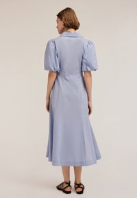 Abito azzurro chiaro, lungo fino al ginocchio, in cotone con collo a camicia, maniche a sbuffo e vita aderente, che presenta una gonna fluttuante e cuciture discrete.