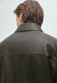 Mörkbrun läderjacka med en slät yta, stor krage och synliga sömnadsdetaljer. Har en avslappnad passform och en minimalistisk design.