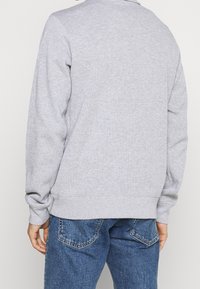 Grauer Pullover mit Rippbündchen an Ärmeln und Saum, mit weicher Textur und schlichtem Design. Wird mit blauen Jeans getragen, Rückansicht gezeigt.
