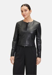 Czarna skórzana kurtka z okrągłym dekoltem, zamek błyskawiczny z przodu i dwoma bocznymi kieszeniami. Gładka tekstura i dopasowany krój. Noszona na czarnych spodniach.