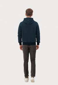 Marineblå hættetrøje i blødt stof med snørelukning i hætten og ribbede manchetter, parret med grå slim-fit bukser og hvide sneakers.