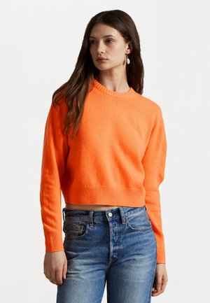 Helle orange, kurz geschnittene Sweater mit rundem Ausschnitt und gerippten Bündchen, kombiniert mit blauen Jeans. Glatte Textur und figurbetonter Schnitt.