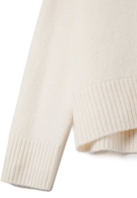 Manche et ourlet de pull en maille blanc cassé avec de larges poignets côtelés et un tissu doux et texturé.