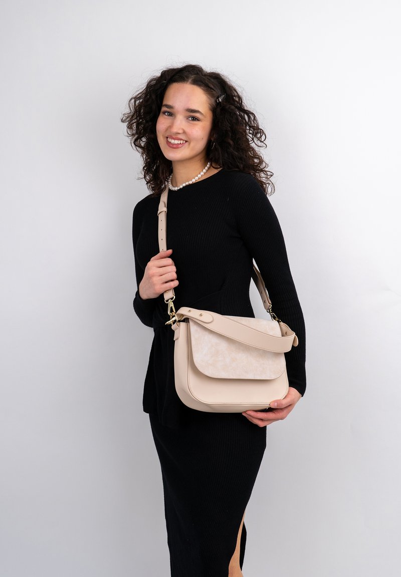 Beige crossbody-väska med en slät läderpanel, texturerad lucka, justerbar rem och detaljer i guld.