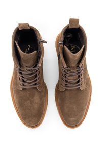 Un par de botas de ante marrón con cordones y cremalleras laterales, con suelas de goma beige, vistas desde arriba sobre un fondo blanco.