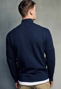 Pulover tricotat bleumarin cu un model texturat, în formă de fagure. Guler înalt și manșete strâmte, asociat cu un tricou alb, design casual.