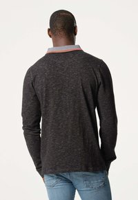 Chemise à manches longues gris foncé avec une finition texturée, présentant un col contraste en bleu clair avec des rayures rouges. Le design comprend un ourlet droit.