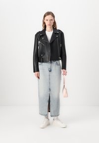 Svart skinnmotorsykkeljakke med glidelåser, kombinert med en lys blå denim maxi skjørt med en frontspalte. Hvite sneakers og en rosa veske.