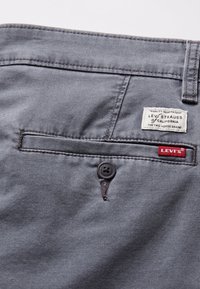 Poche arrière d'un pantalon Levi's gris avec un bouton noir, une boucle de ceinture cousue et des étiquettes de marque Levi's blanches et rouges visibles.