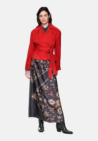 Red suede wrap jacket with a tie waist, paired with a long black skirt featuring a colorful floral pattern and black ankle boots.