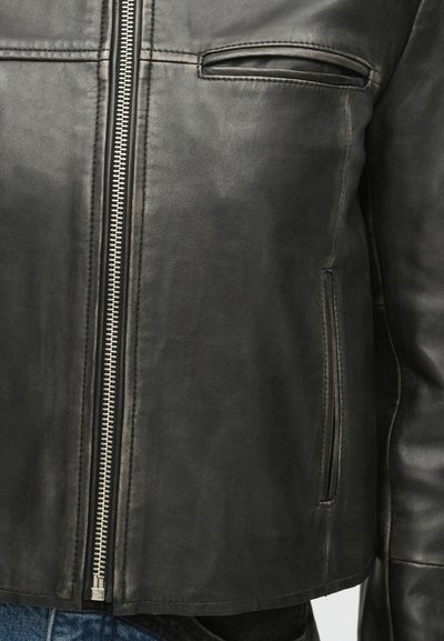 Giacca in pelle nera con cerniera frontale, due tasche laterali e una texture liscia. Cuciture evidenti lungo le cuciture e i bordi.