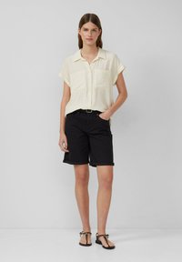  Lichtgele shirts met korte mouwen en twee voorzakken, gecombineerd met zwarte shorts met opgerolde mouwen en platte, zwarte sandalen. Eenvoudig ontwerp en texturen.
