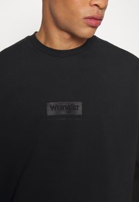 Felpa nera in cotone, con collo rotondo, caratterizzata da un sottile logo Wrangler grigio sul petto, dal texture morbida.