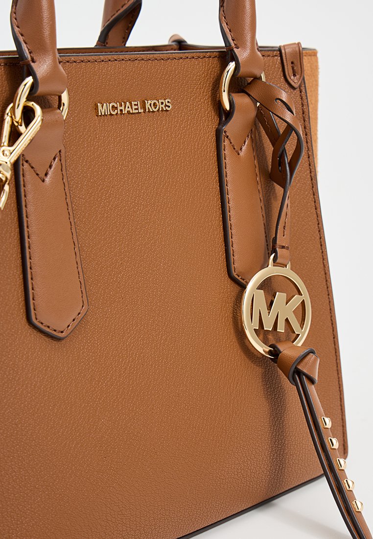 Bolso de mano de cuero marrón con textura de guijarro y herrajes dorados, que presenta una etiqueta de logo redondeada y un diseño estructurado. Mangos acampanados y costuras decorativas.