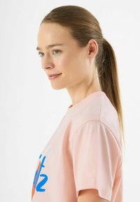 Lichtroze katoenen t-shirt met blauwe en oranje grafische tekst. Klassieke ronde hals, korte mouwen en een ontspannen pasvorm.