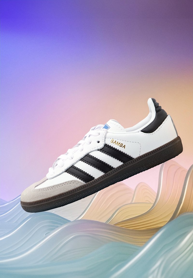 White sneaker with black accents, three black stripes, and a grey suede toe. Features a textured black rubber sole and gold "SAMBA" logo.