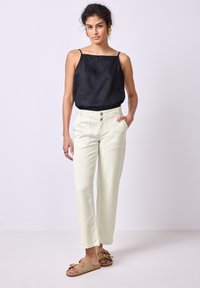 Černý lněný top bez rukávů v kombinaci se světle krémovými širokými kalhotami s dvěma předními kapsami a béžovými sandály s mašlí.