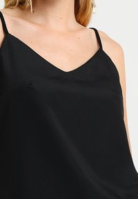 Schwarzes Camisole-Top aus glattem Stoff, mit dünnen Trägern und V-Ausschnitt, locker sitzend und mit minimalen Nähten.
