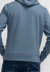 Mikina s kapucí v barvě prachově modré, vyrobená z měkké látky. Má žebrované manžety a lem, a kapsu typu klokánek vpředu.