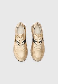 Une paire de baskets métalliques dorées avec des lacets beiges et des accents latéraux noirs, posée à plat sur un fond blanc.