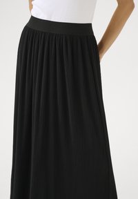 Jupe plissée noire dotée d'une taille lisse et d'une texture verticale, offrant une silhouette fluide. Parfaite pour différentes occasions.