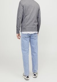 Felpa grigia con polsini e orlo a costine, indossata sopra una camicia a righe. Jeans azzurri dal taglio morbido e sneakers grigie completano il look.