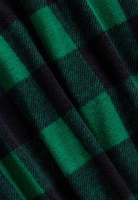 Kostkovaná deka s zelenými a černými čtverci, vyrobená z měkké, texturované látky s vlněným vzhledem a jemnými diagonálními pruhy.