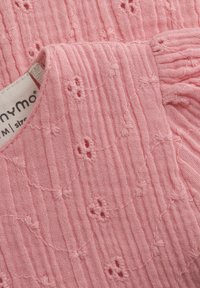 Pink textured fabric with a ribbed pattern, featuring small embroidered flowers. Tag visible indicating size and brand.