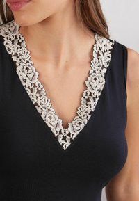 Schwarzes Oberteil mit tiefem V-Ausschnitt und floralem Spitzenbesatz in Beige. Glatte Textur mit figurbetontem Design, das das Detail des Ausschnitts betont.