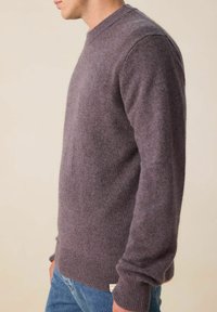 Pull en laine violet avec un col rond, des poignets et un ourlet côtelés. Texture douce, silhouette ajustée, porté sur un jean en denim.