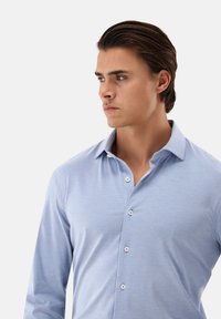 Camicia a maniche lunghe azzurro chiaro con colletto classico, caratterizzata da una texture liscia, apertura anteriore con bottoni e un leggero splendore.