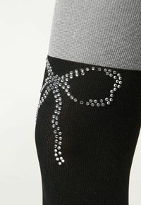 Sorte og grå benvarmere med en struktureret finish, prydet med et rhinestone sløjfe-design i sølv på den sorte sektion.