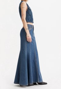 Jeansmaxikjol med en utsvängd silhuett, ljusblå färg, synliga söm detaljer och dragkedjestängning framtill, parat med en kort denimväst.