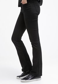 Svarta utsvängda jeans tillverkade av en stretchig bomullsmix, med en slät yta, minimala sömmar och två sidofickor. Matchad med svarta sneakers som glider på.