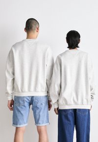 Felpe grigie con polsini e orlo a coste, indossate da due persone. Una in pantaloni corti di jeans, l'altra in jeans blu larghi. Design minimalista.
