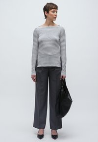 Hosszú ujjú, fekete-fehér csíkos felső, szürke, bő szárú nadrággal párosítva. A modell egy texturált fekete táskát tart, és fekete magassarkút visel.